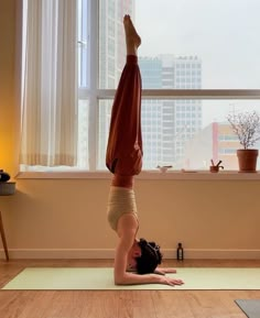 a person doing a handstand on a yoga mat in front of a window