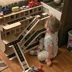 a young boy playing with toy cars on the floor in front of a bookcase