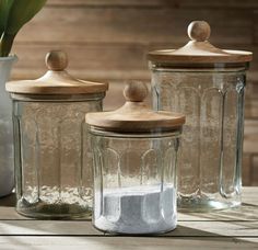 three glass jars with wooden lids on a table