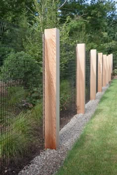 a row of wooden posts on the side of a fenced in area next to grass and trees