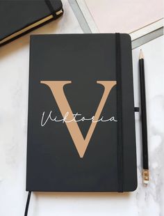 a black notebook with the letter v on it next to a pen and notepad