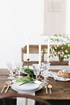 a wooden table topped with white flowers and plates covered in greenery next to candles