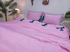 a bed with pink sheets and pillows in a bedroom next to a potted plant