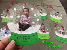 a hand holding up a snow globe with a baby in it and many other ornaments on the table