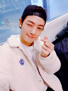 a young man in a white jacket and black hat holding something up to his face