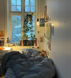 an unmade bed sitting in front of a window next to a desk with a lamp on it