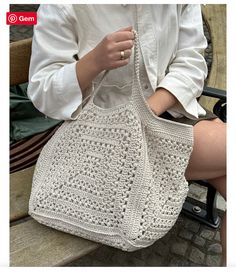 a woman is sitting on a bench holding a crocheted handbag in her hands