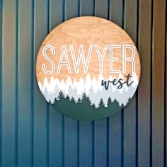 a wooden sign that says sawyer west on the side of a blue building with trees