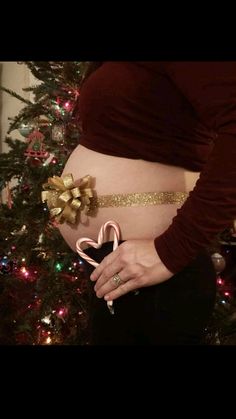 a pregnant woman holding a candy cane in front of a christmas tree with her belly exposed