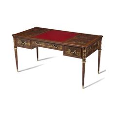 an antique desk with red leather top and gold trimmings on the legs, against a white background