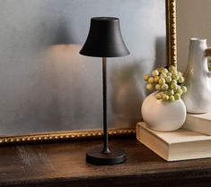 a table with a lamp, vases and books on it next to a mirror