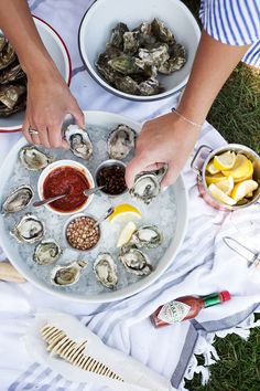 a woman is serving oysters from a platter on the grass with lemon wedges and ketchup