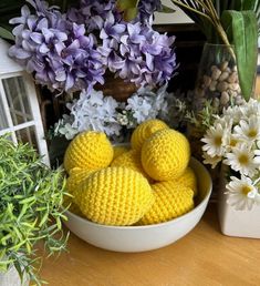 some crocheted balls are in a white bowl on a table next to flowers