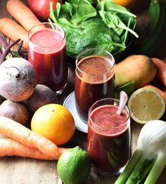 there are many fruits and vegetables on the table with juices in glasses next to each other