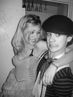 two young people standing next to each other in a black and white photo, one wearing a hat