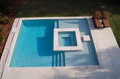 an aerial view of a swimming pool with lounge chairs on the side and grass in the background