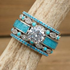 a ring with turquoise and white stones on it sitting on top of a piece of wood