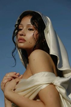 a woman in a white dress with her hands on her chest and the sky behind her