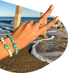 a woman's hand with two bracelets on it and the ocean in the background