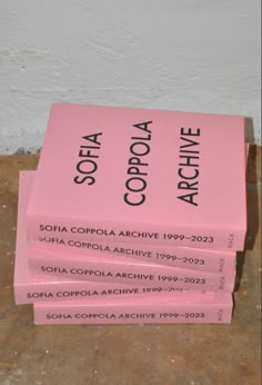 four pink books stacked on top of each other in front of a white wall with black writing