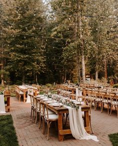 an outdoor dining area with wooden tables and white linens on them, surrounded by greenery