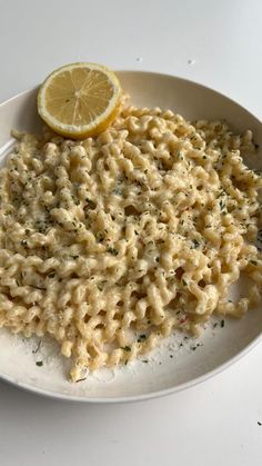 a white plate topped with macaroni and cheese next to a slice of lemon