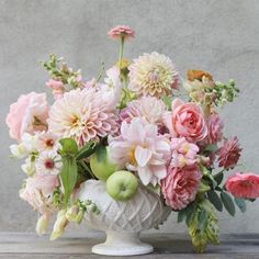 a white vase filled with lots of pink flowers and apples on top of a table