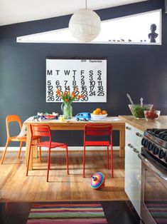 a kitchen table with chairs and a calendar on the wall above it, in front of a stove