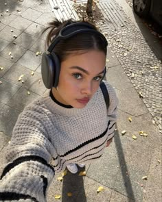 a woman with headphones on taking a selfie in front of a tree and parked car