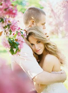 a young man and woman embracing each other in front of pink flowers on the tree