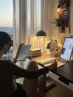 a woman sitting in front of a computer on top of a desk next to a window