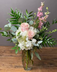 a vase filled with flowers and greenery on top of a wooden table