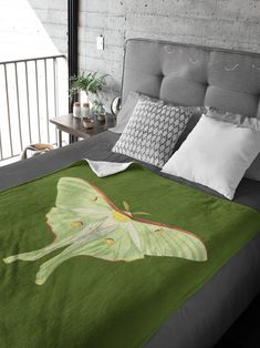 a bed with a green blanket on top of it next to pillows and a plant