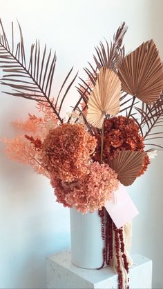 a white vase filled with lots of different types of flowers and leaves on top of a table