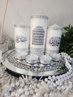 four candles with arabic writing on them sitting on a tray surrounded by beads and greenery