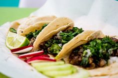 three tacos on a plate with limes and radishes