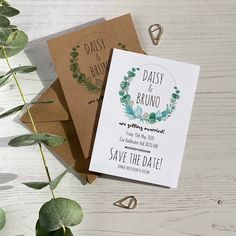 two wedding save the dates cards on top of each other next to some greenery