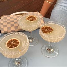 three wine glasses with orange slices in them sitting on a table next to a purse