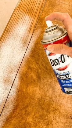 a hand holding a can of spray paint on top of a wooden table