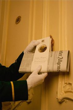 a person in white gloves holding up a newspaper