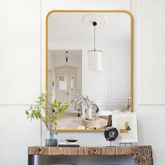 a mirror sitting on top of a wooden table next to a vase filled with flowers