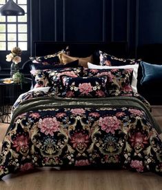 a bed covered in black and pink flowers on top of a wooden floor next to a window