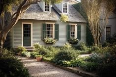 a house with green shutters and plants in the front yard on a sunny day