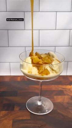 an ice cream sundae with caramel syrup being poured into it on a wooden table