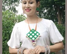 a woman in a white shirt holding two bracelets and a green square shaped pendant