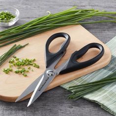 a cutting board topped with green onions and two pairs of scissors next to chopped chives