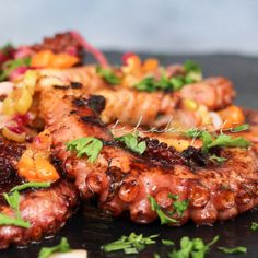 grilled octopus with vegetables and herbs on a black plate