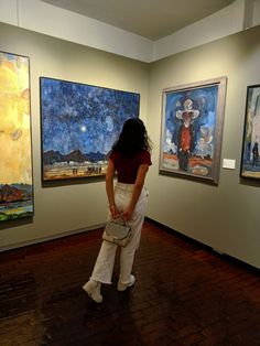 a woman looking at paintings on display in an art gallery with wooden floors and white walls