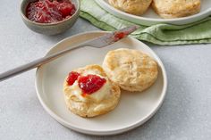 two biscuits with jam on them sit on a plate next to a bowl of jelly