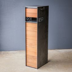 a tall metal mailbox sitting on top of a cement floor next to a wall